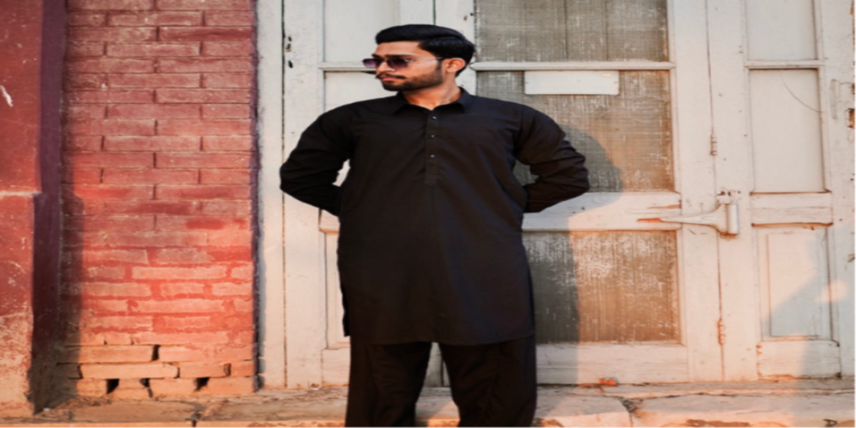 Man in a black outfit standing against a brick wall and old door.