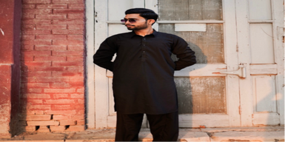 Man in a black outfit standing against a brick wall and old door.